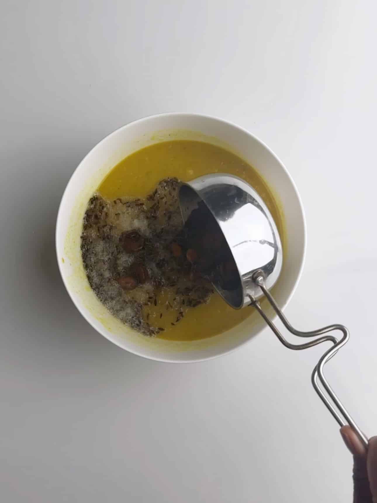 Adding the hot oil with cumin and sliced garlic to the cooked dhal