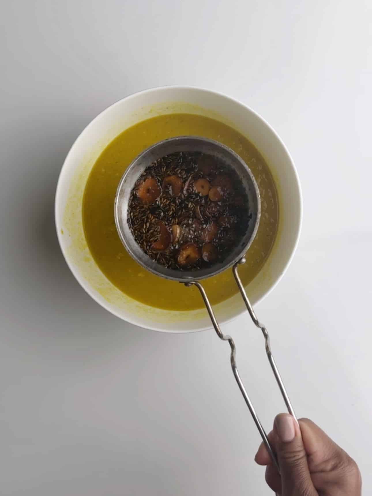 Holding the hot oil with geera and garlic over the cooked dhal.