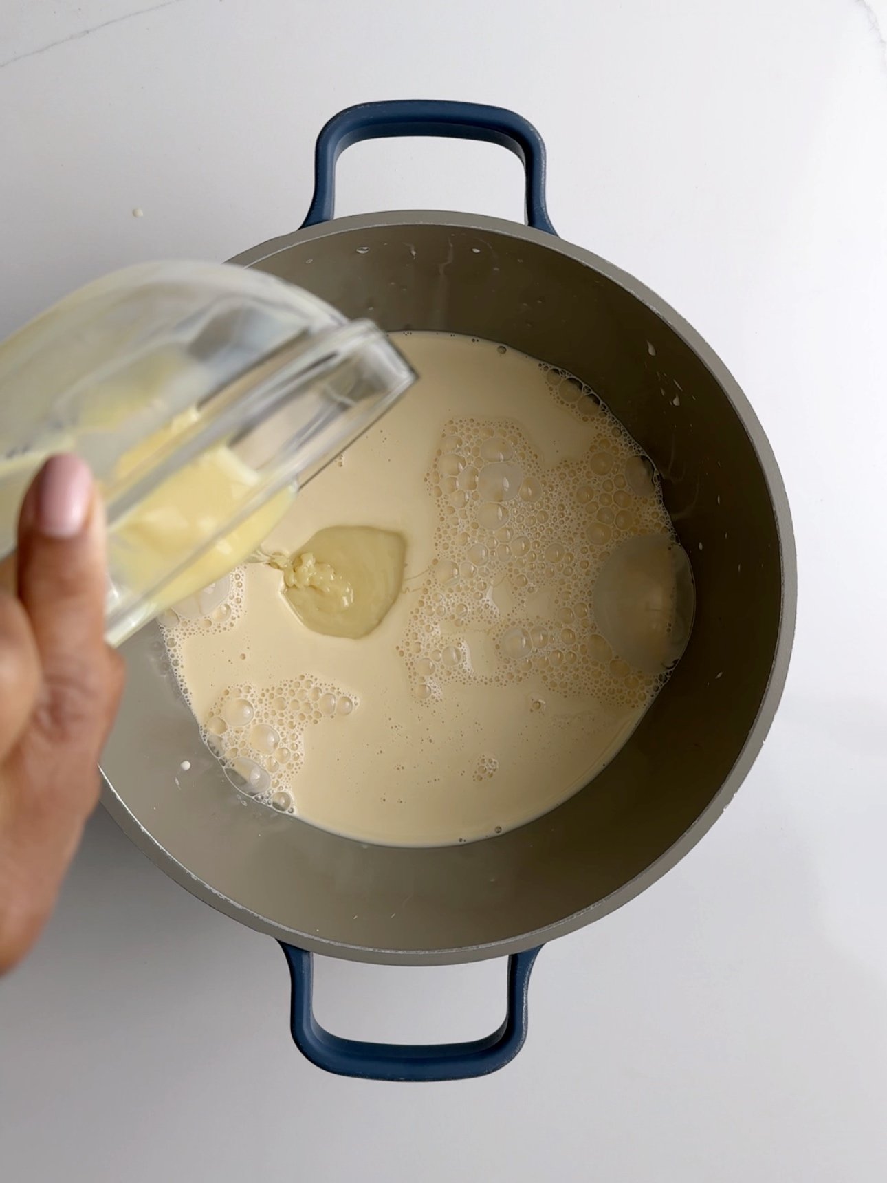 Adding evaporated milk and condensed milk to a grey saucepan to make baked custard