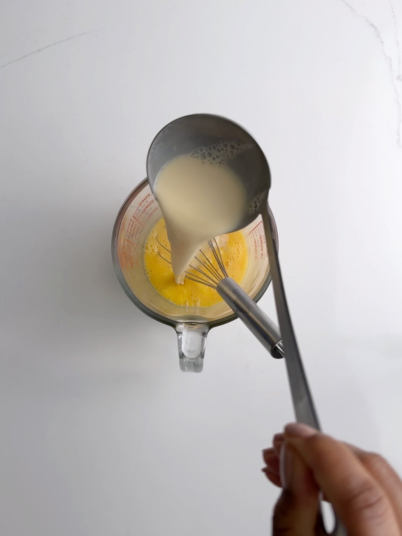 Pouring hot milk into whisked eggs to temper them.