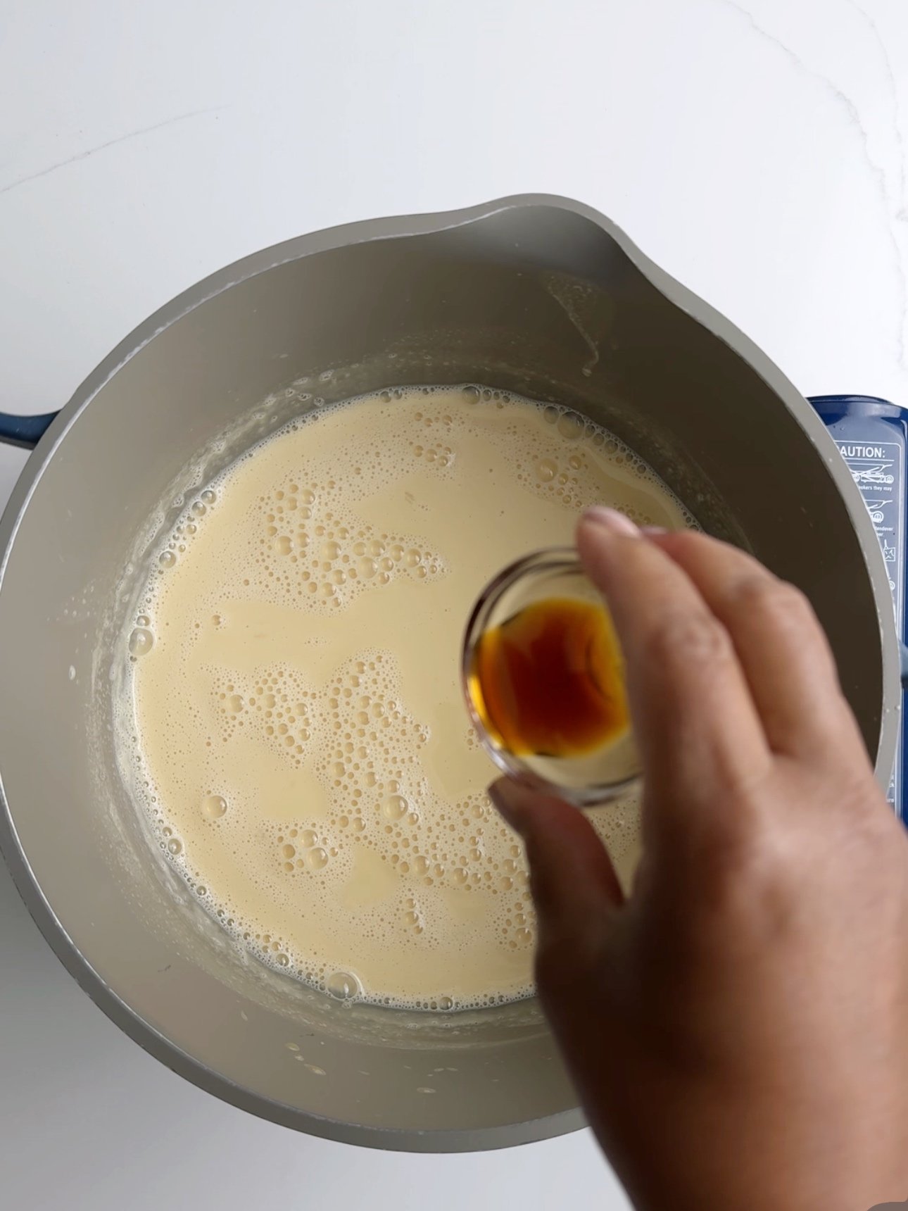 Pouring vanilla extract into a saucepan of warm custard. 