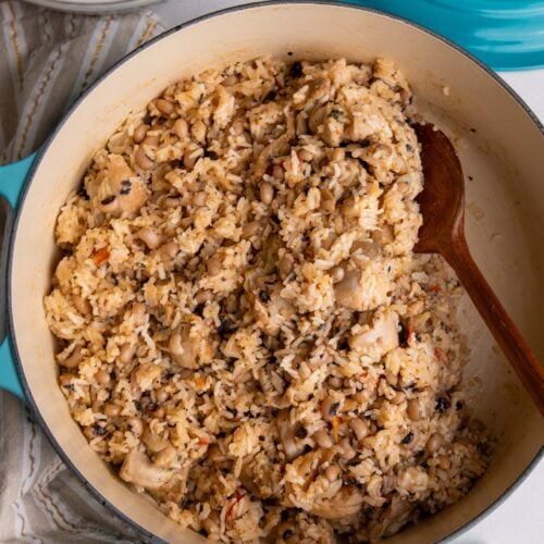 Overhead view of finished chicken cook-up rice in a Dutch oven with a wooden spoon.