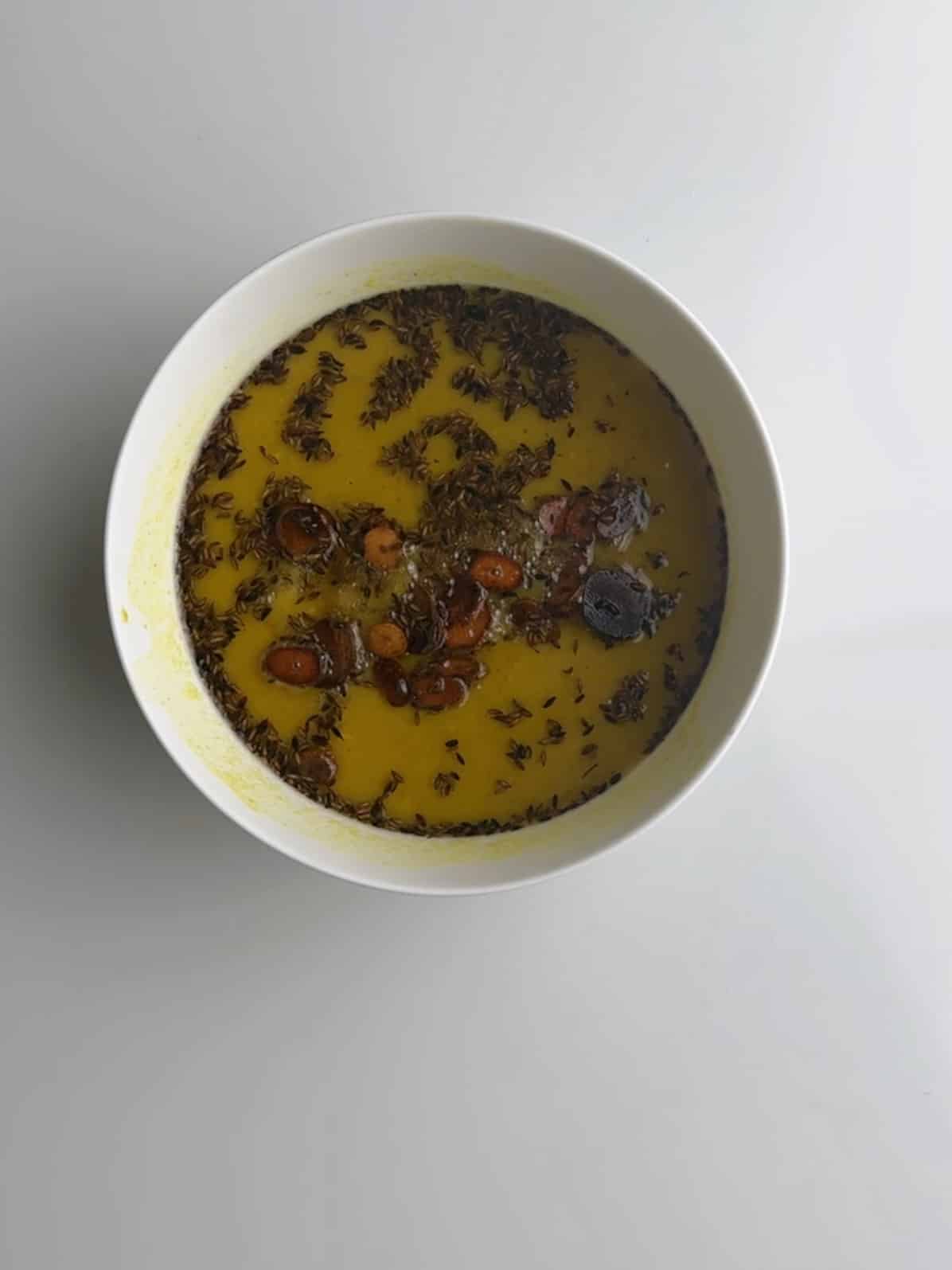 A white bowl with dhal and the visible oil, garlic and turmeric.