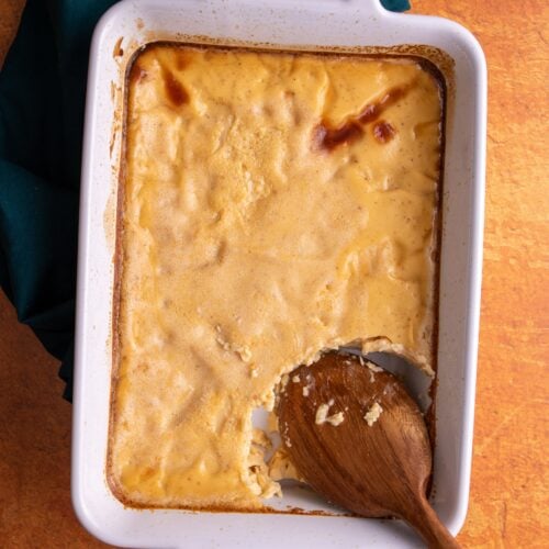 Baked custard in a white rectangular dish with handles on both ends on an orange colored background and a green napkin on the left.