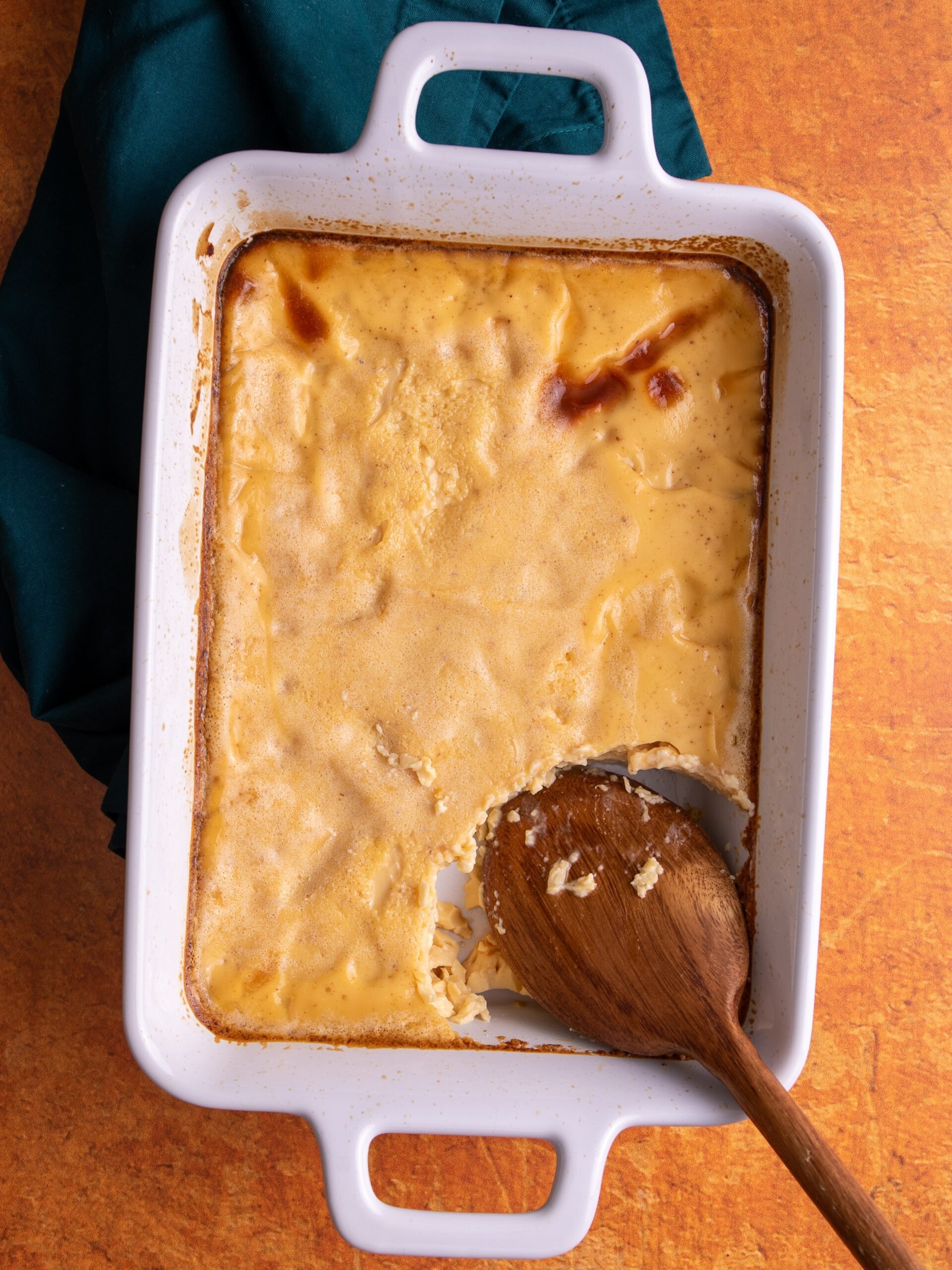 Baked custard in a white rectangular dish with handles on both ends on an orange colored background and a green napkin on the left.