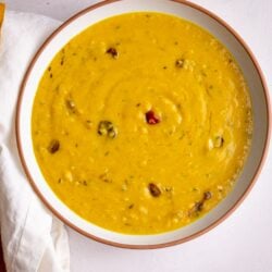 Dhal in a while bowl with a brown rim on a white background.