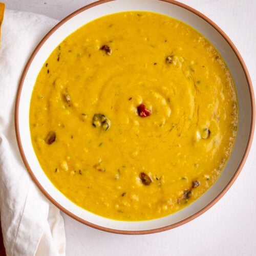 Dhal in a while bowl with a brown rim on a white background.