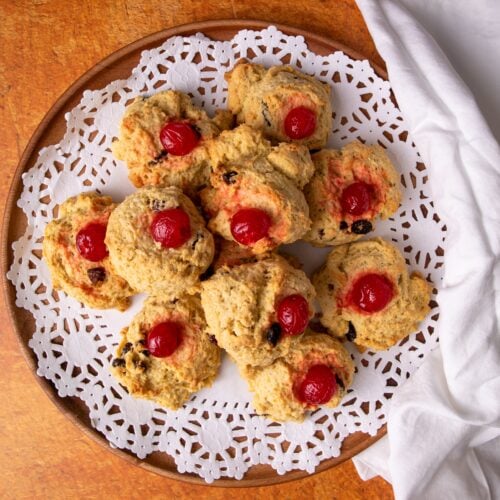 Guyanese coconut buns on a while doily on a wooden plate. The plate is on a brown brick background and a white cotton napkin is to the right.