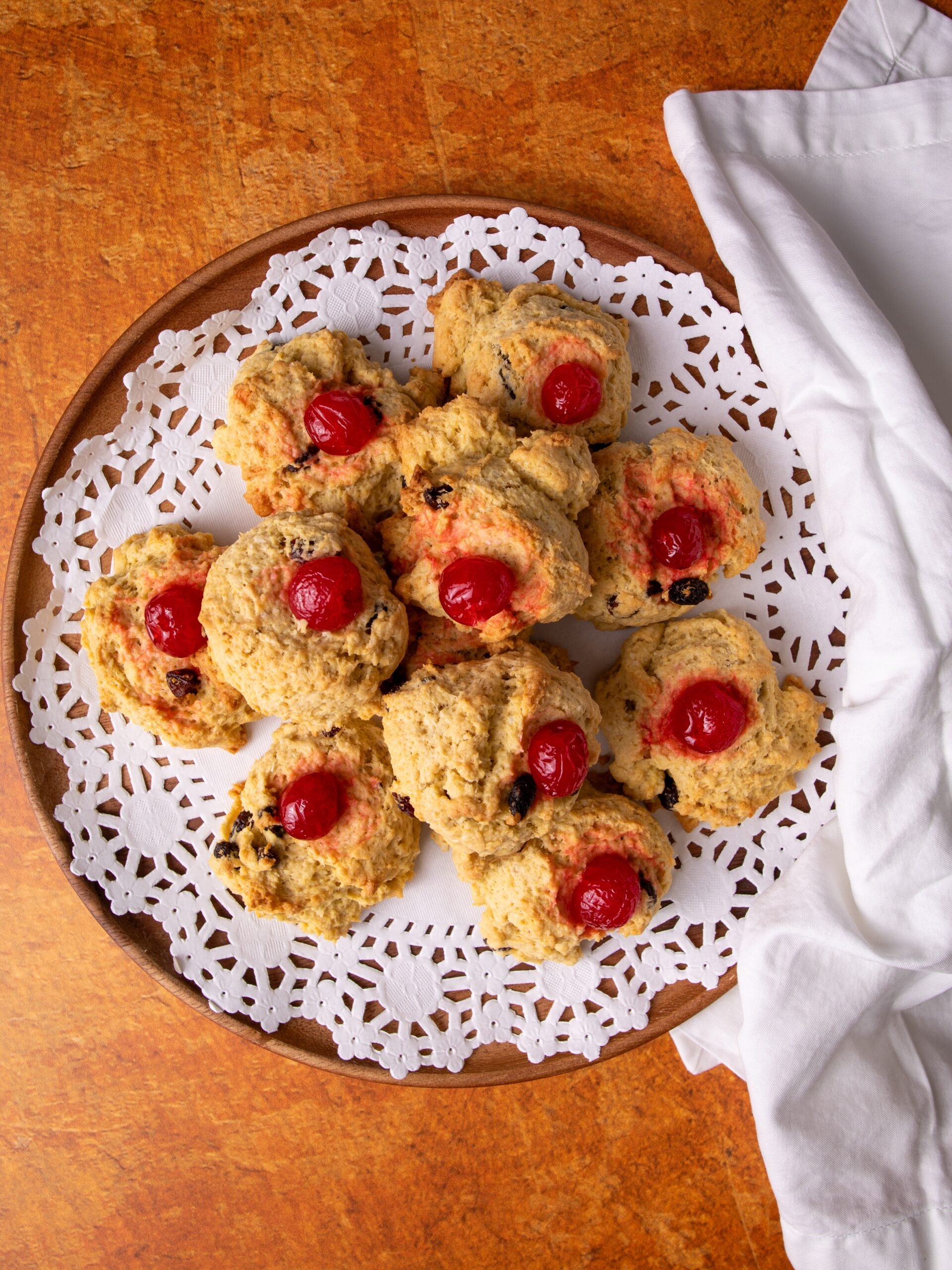 Guyanese coconut buns on a while doily on a wooden plate. The plate is on a brown brick background and a white cotton napkin is to the right.