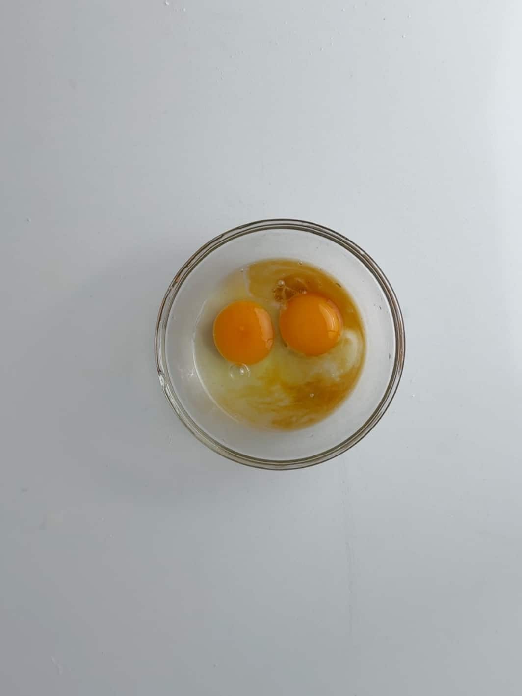 Eggs, vanilla extract and almond extract in a glass bowl on a white counter