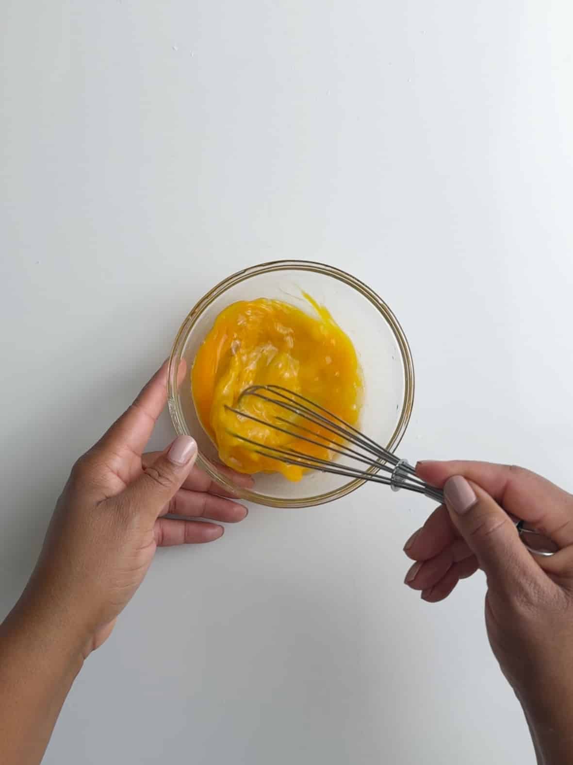 Whisking eggs in a glass bowl on a white background