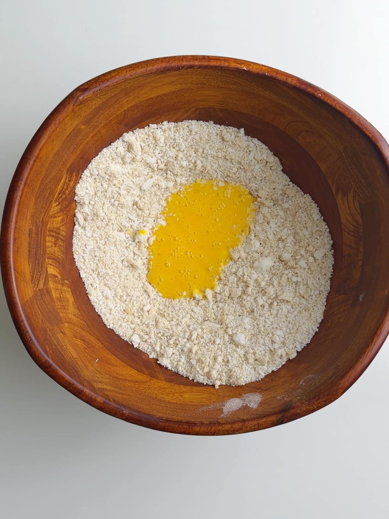 Dry ingredients in a brown bowl with whisked eggs on top for coconut buns.