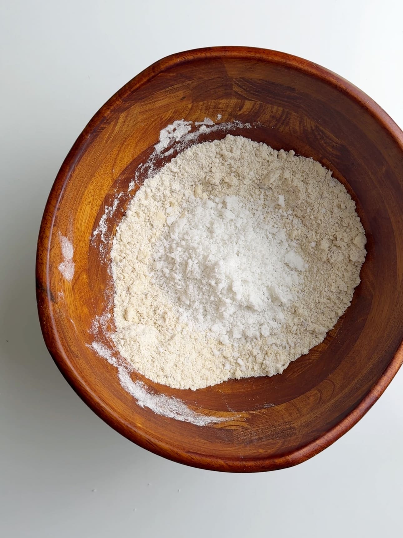 Coconut and other dry ingredients in a wooden bowl on a white counter. 