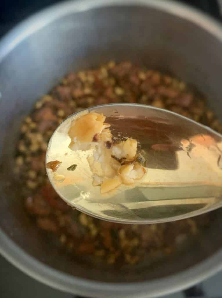a spoon with a mashed black eyed pea over a pot of cook-up rice