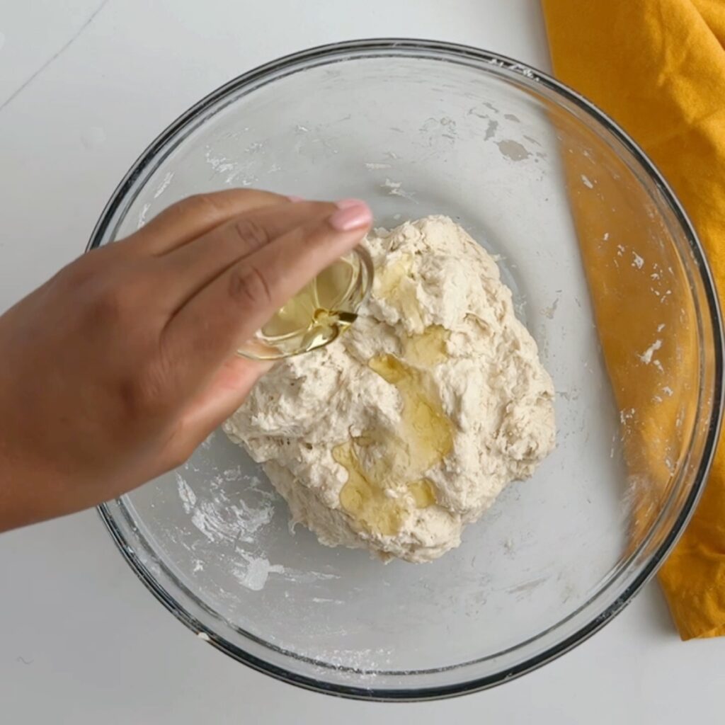 Pouring oil over roti dough in a glass bowl