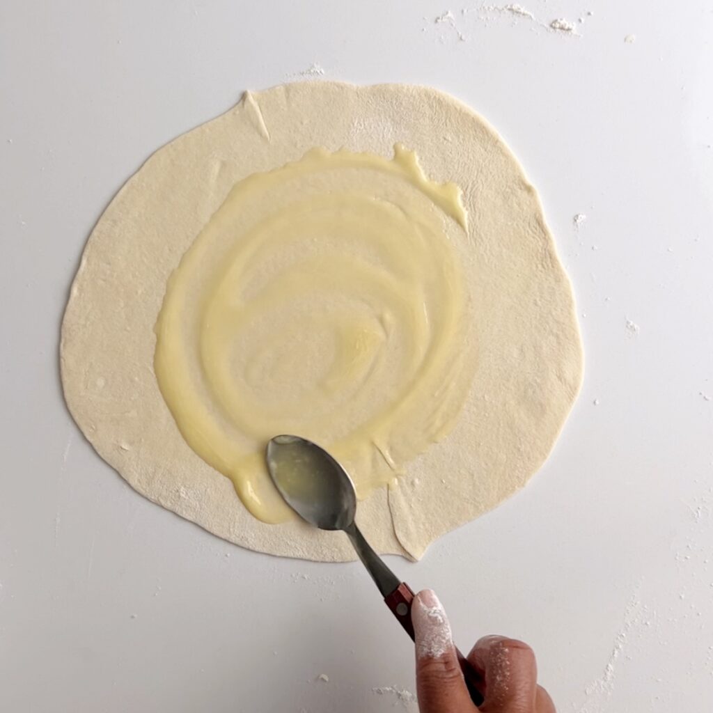 Adding oil to the roti dough using a spoon