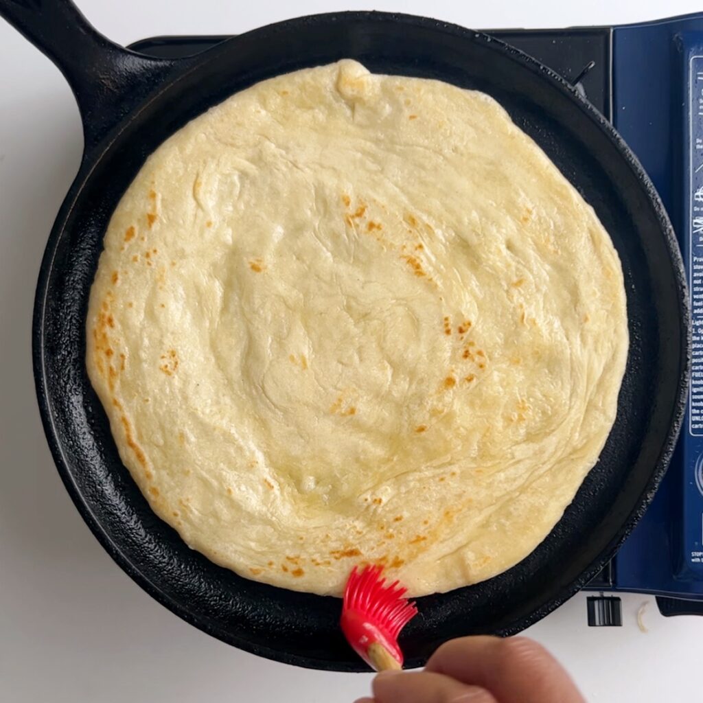 Brushing cooked roti with oil using a red silicone pastry brush
