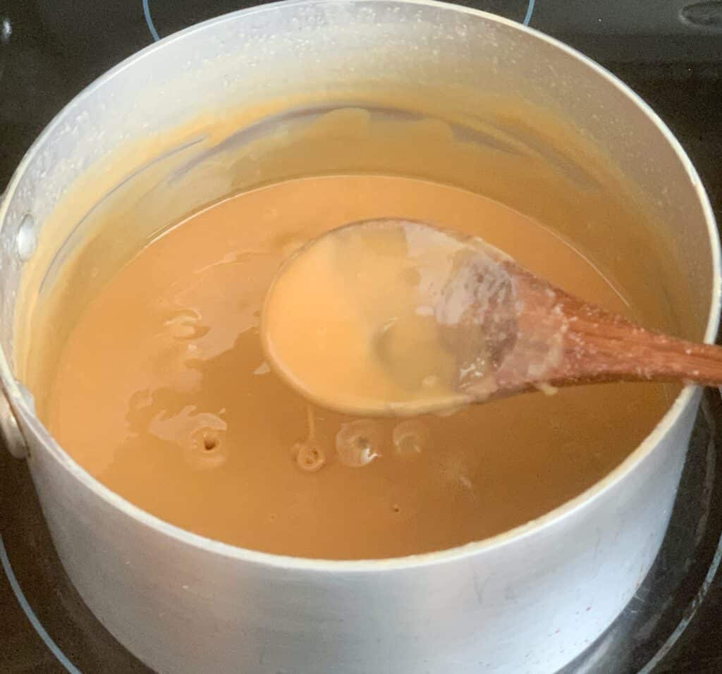 Vanilla fudge in a sauce pan and a wooden spoon over the pot