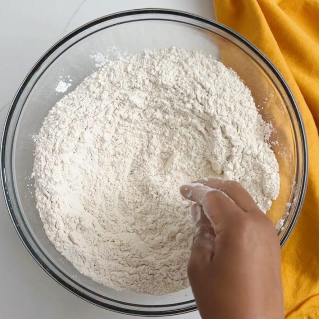 mixing flour, baking powder and salt together with my finger tips in a large mixing bowl with mustard colored napkin to the right of the bowl