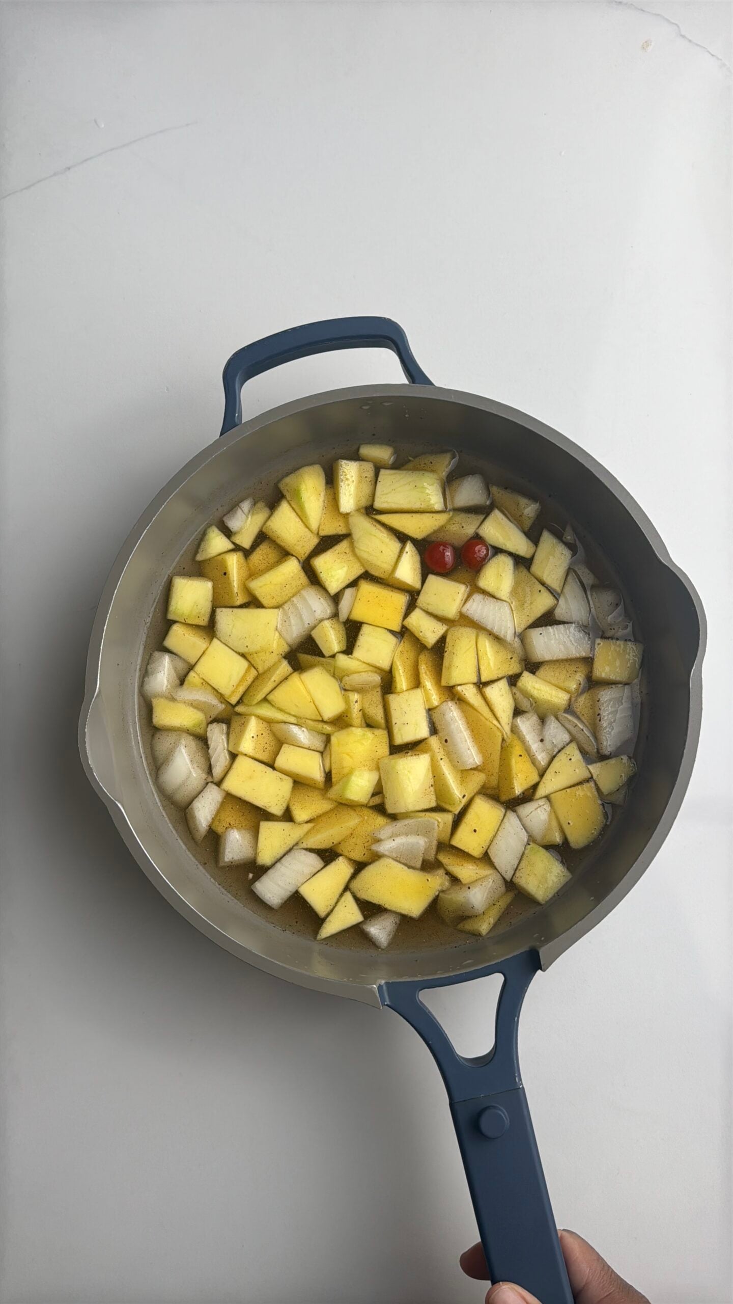 Chunks of green mango, onion, and wiri wiri pepper simmering in a saucepan while making Guyanese mango sour.