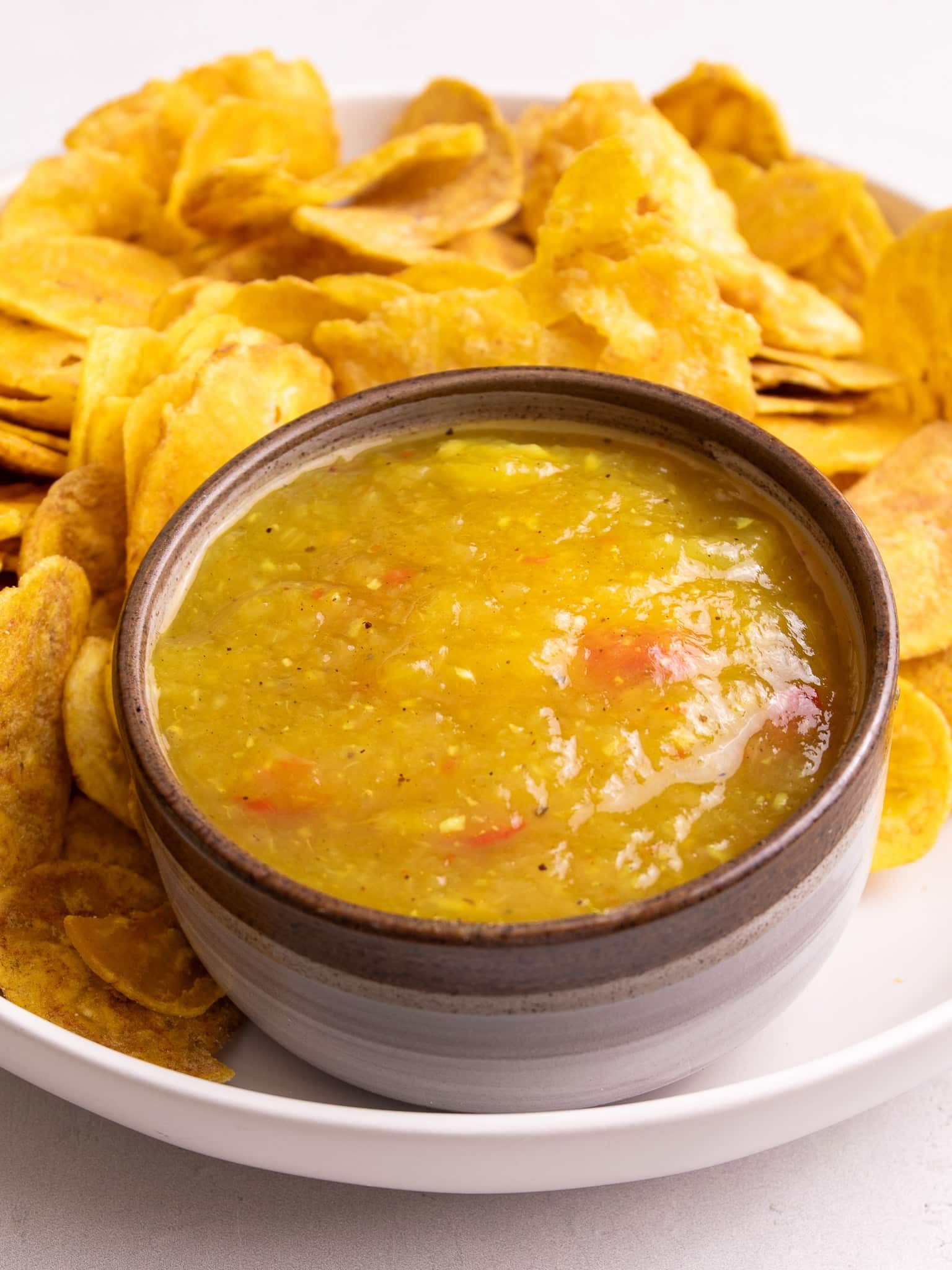 Close up of Guyanese mango sour served with plantain chips and cassava chips on a white plate.