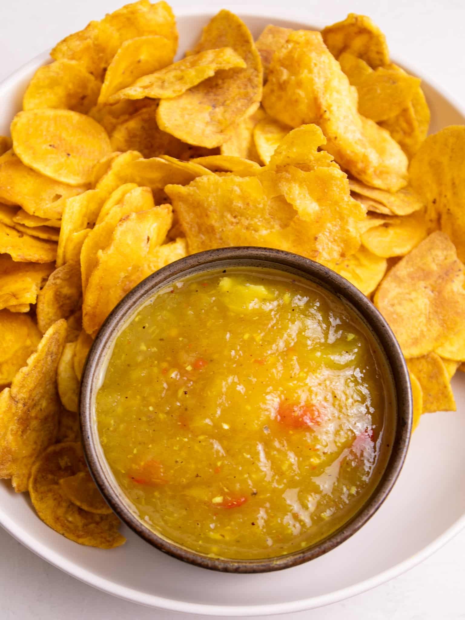 Close up of Guyanese mango sour served with plantain chips and cassava chips on a white plate.