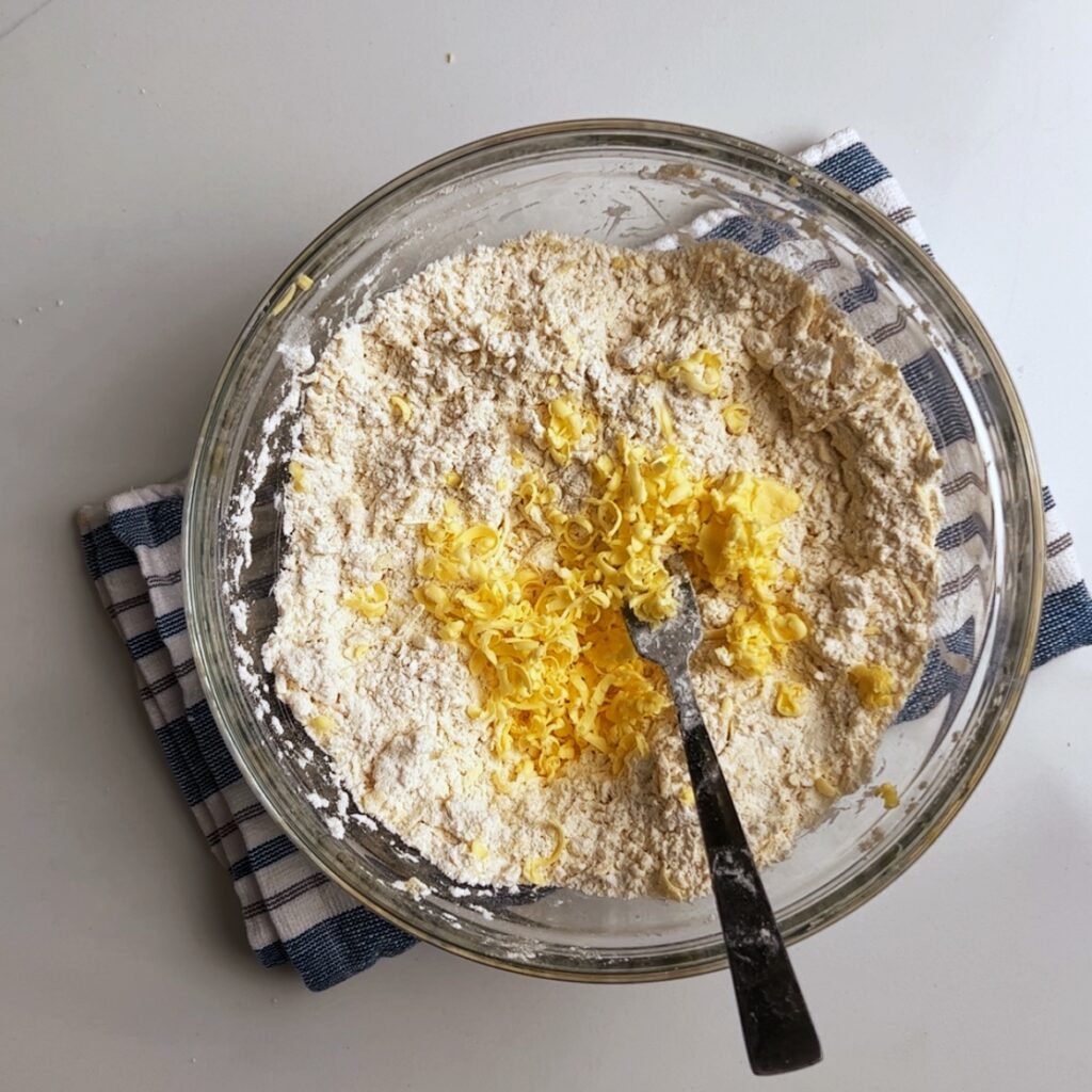 Flour and grated butter in a glass bowl with a fork