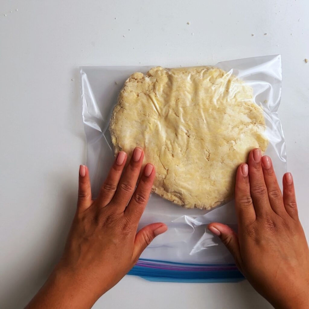 pressing down pastry dough in a ziplock freezer bag with brown hands