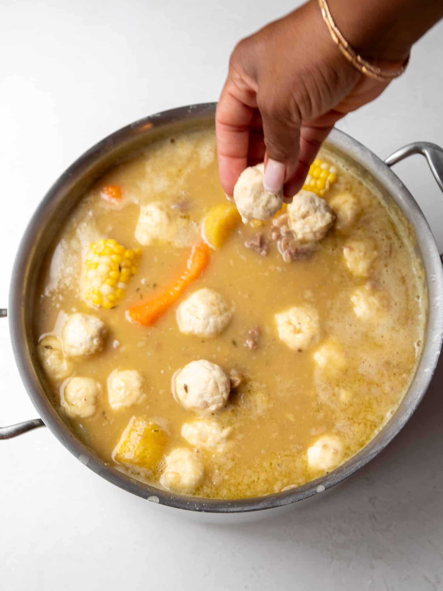 Hand dropping dumplings on top of a simmering pot of Caribbean oxtail soup