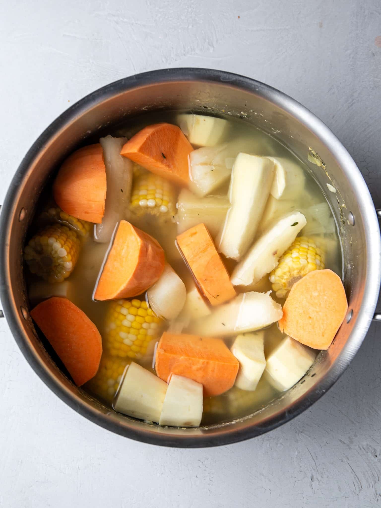 Orange and white sweet potatoes added to the pot of cassava and corn, covered with water