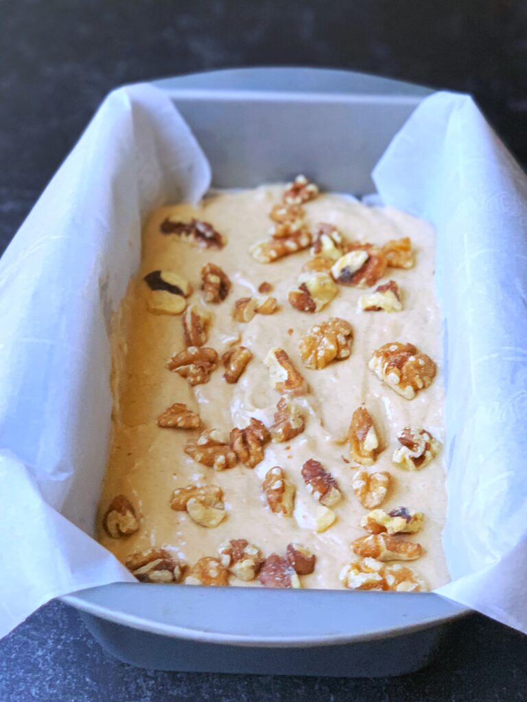 banana bread batter topped with walnuts in a parchment lined loaf pan