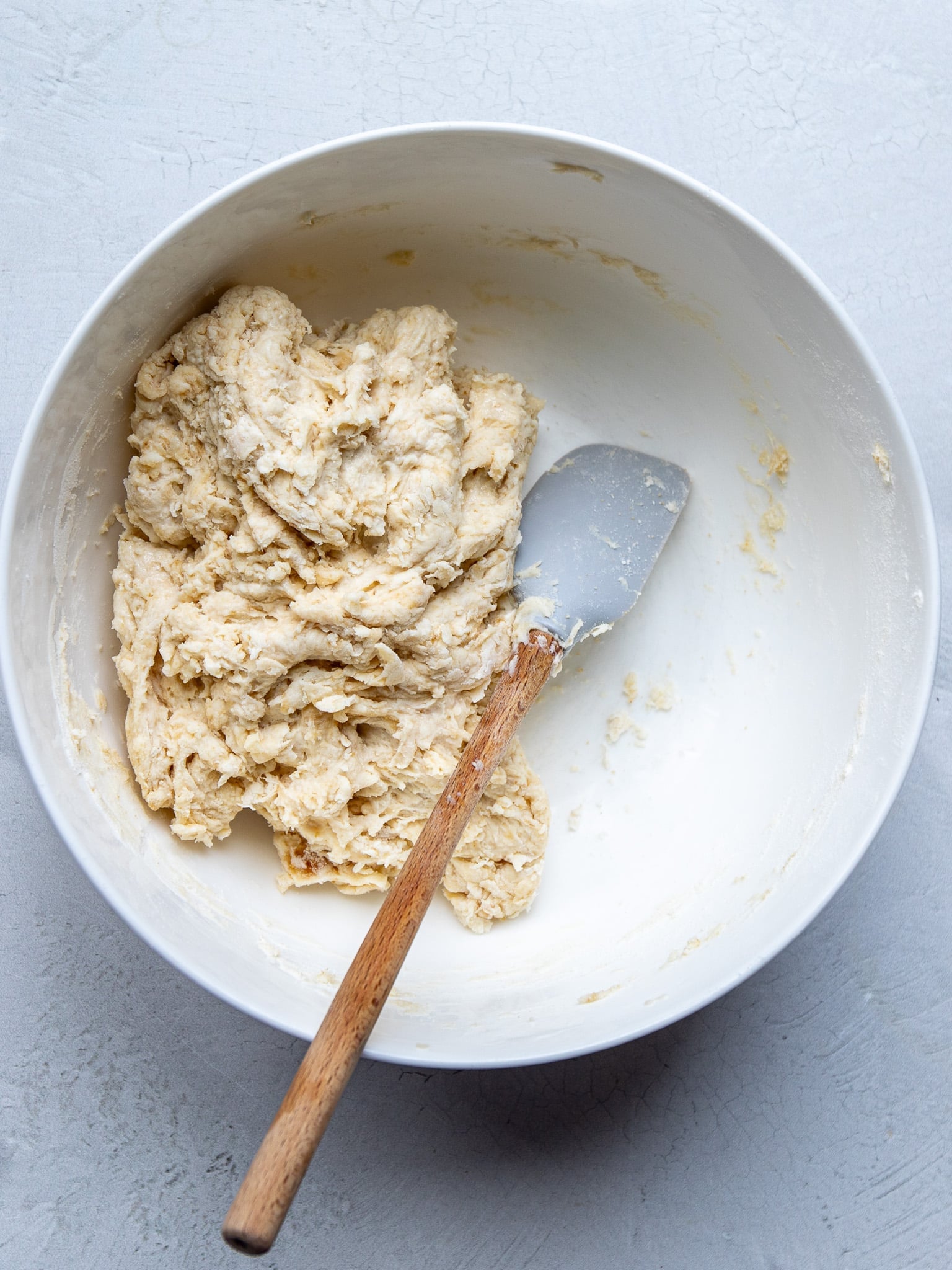 Freshly mixed dumpling dough with a spatula in a white mixing bowl