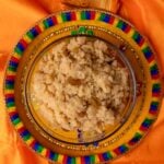 Guyanese parsad in a clear bowl sitting on a multi-colored plate on an orange saree background.