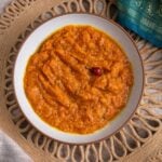 Overhead bowl of Guyanese sautéed pumpkin with a wiri wiri pepper, on a woven placemat with a teal sari
