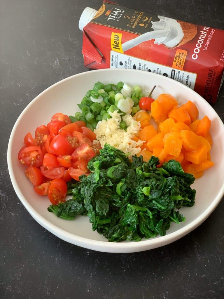 a bowl of callaloo cook-up ingredients in a bowl with a container of coconut milk in the background.