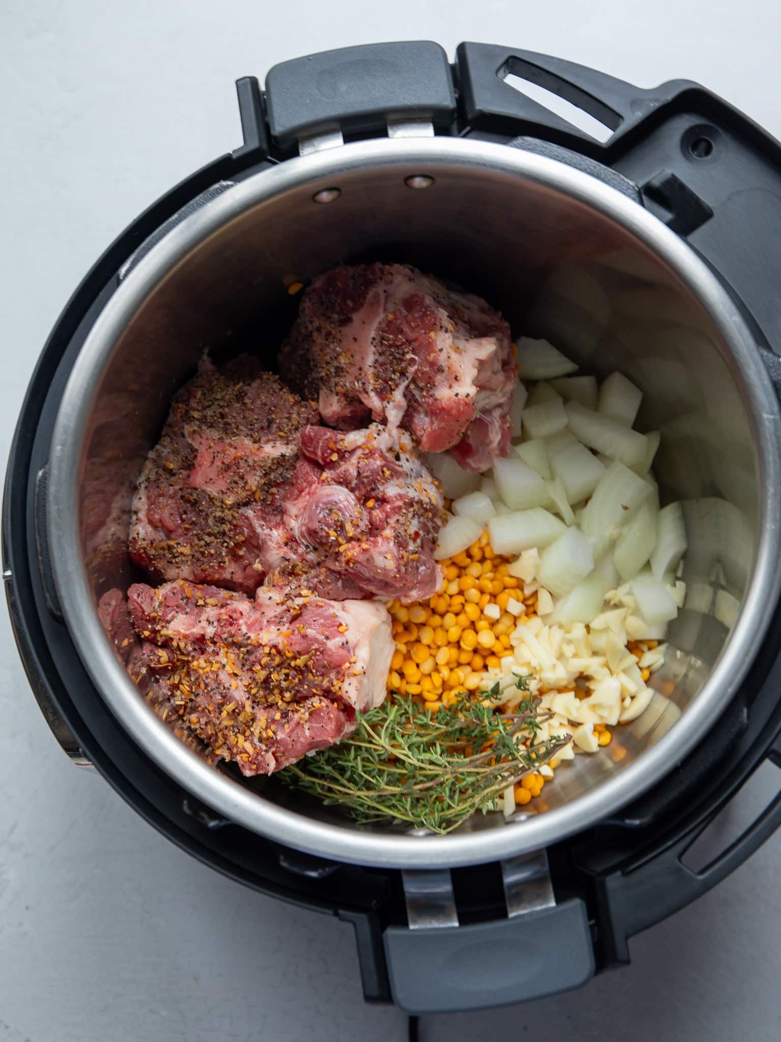 Seasoned oxtail, yellow split peas, diced onion, chopped garlic, and fresh thyme in an Instant Pot before pressure cooking