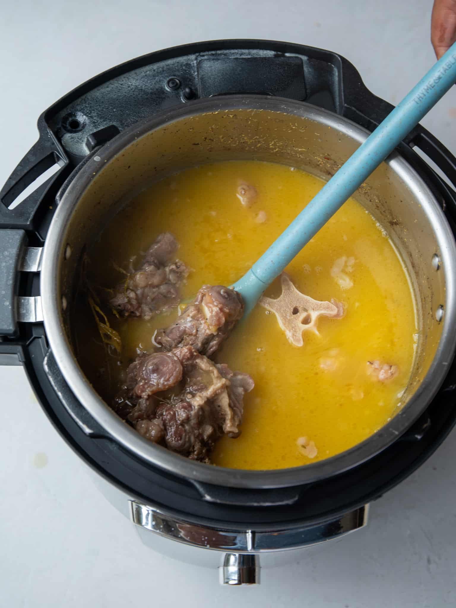 Tender pressure-cooked oxtail in golden split pea broth in an Instant Pot, showing the round oxtail bone