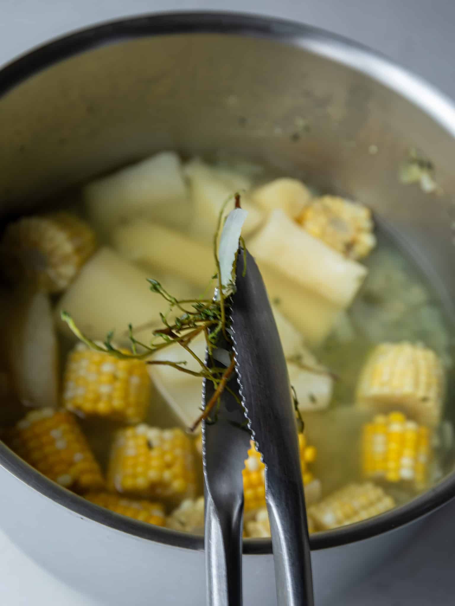 Lifting thyme stems out of the soup pot with tongs before adding the oxtail