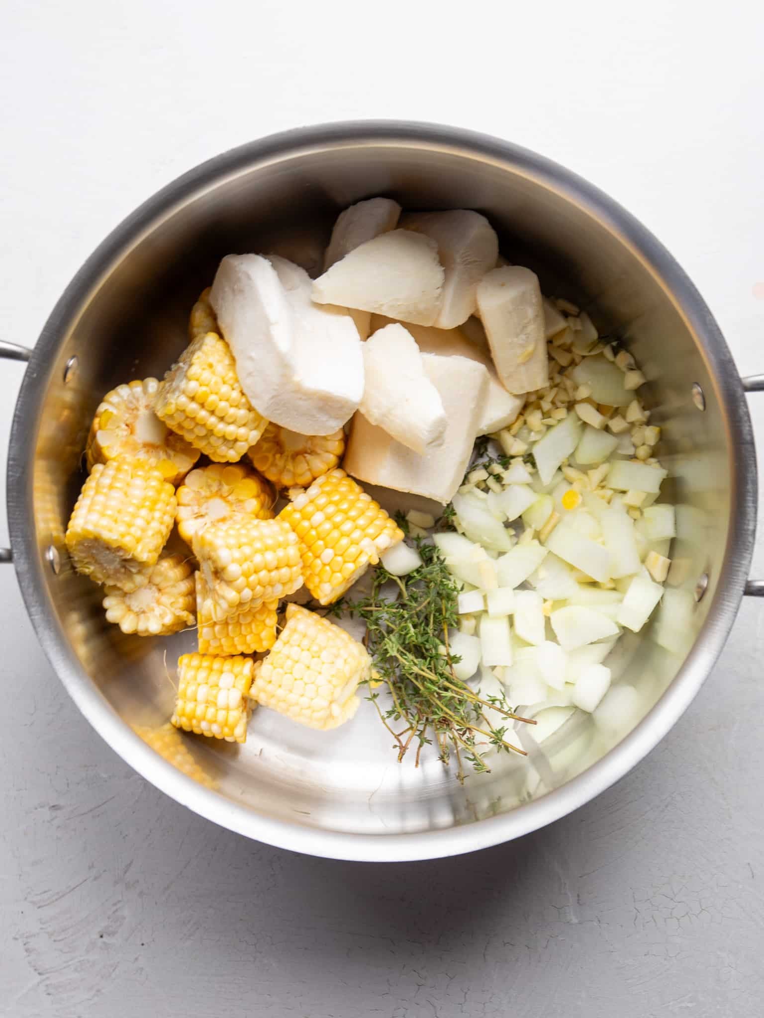 Frozen cassava, corn on the cob rounds, diced onion, chopped garlic, and fresh thyme in a large stockpot