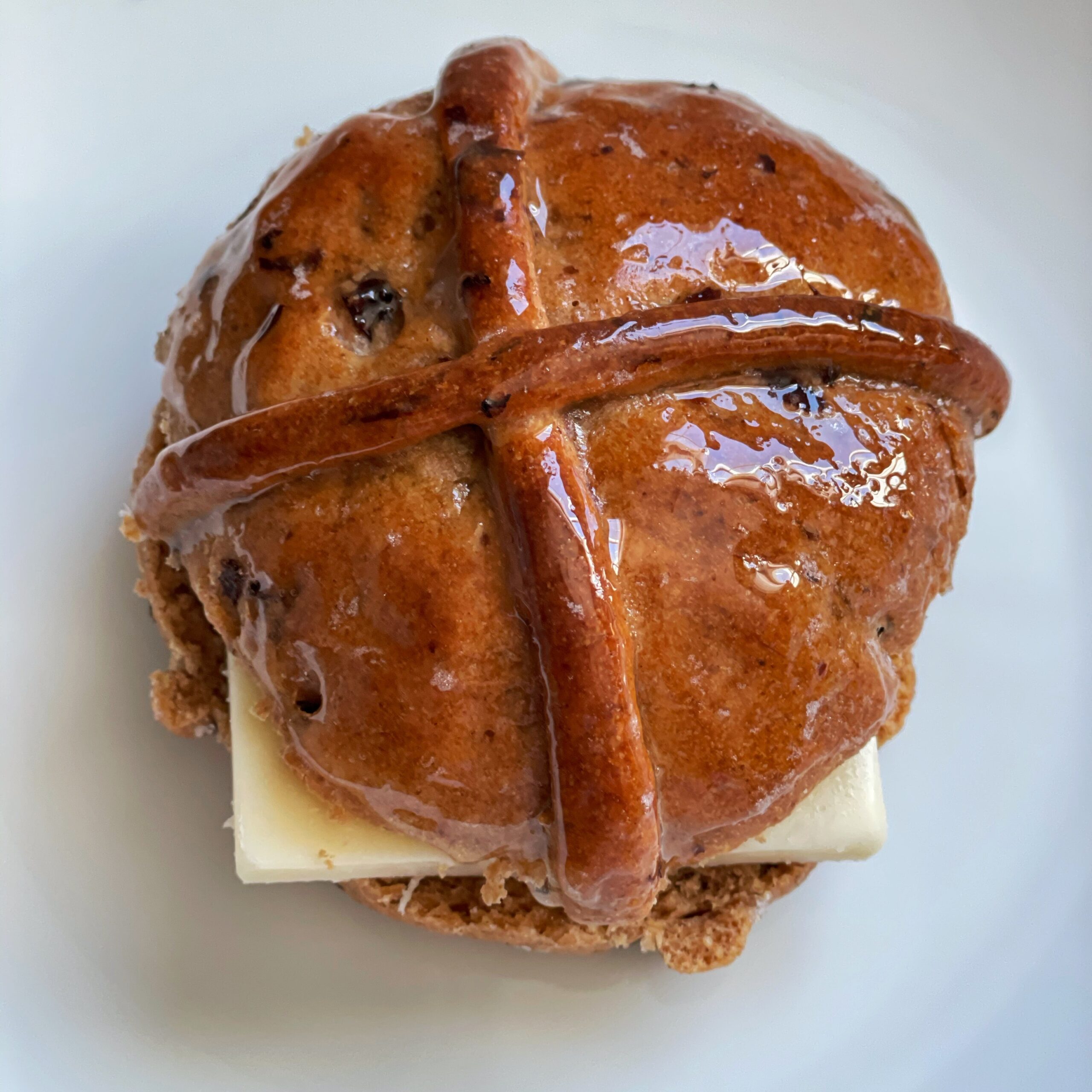 Cross buns on a white surface with a slice of cheese peeking out