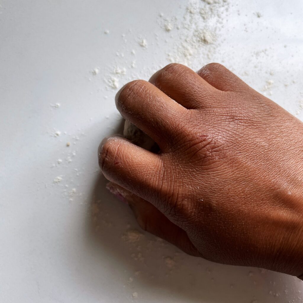 a brown hand rolling dough on a white floured counter