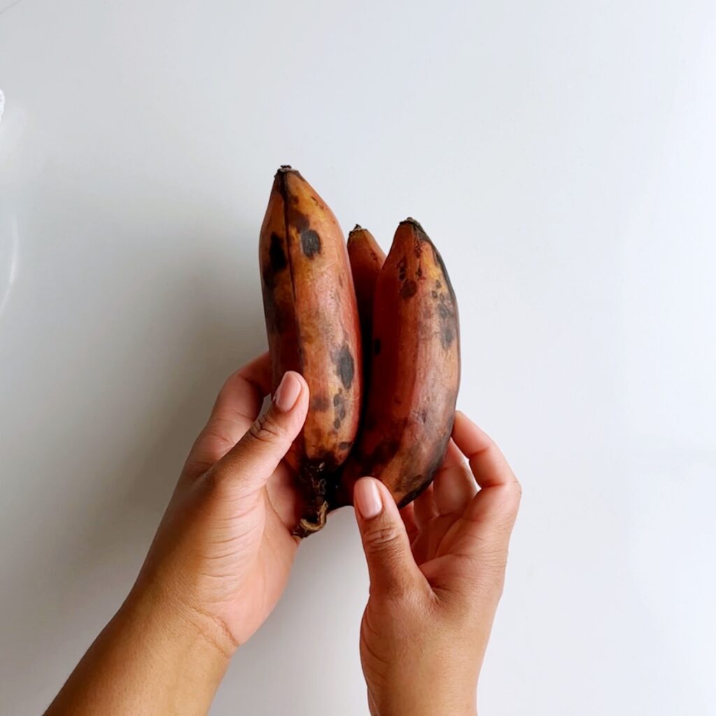 three red bananas in brown hands