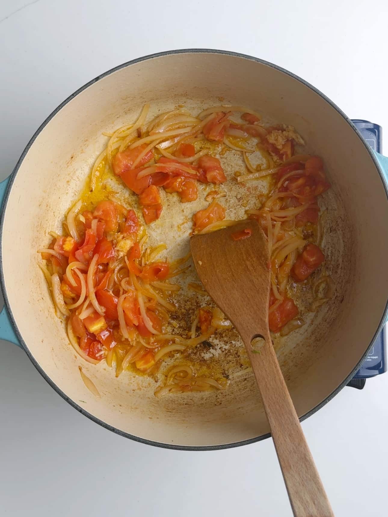 Sautéeing onions, tomatoes, garlic in a pan with a wooden spoon to make Guyanese pumpkin