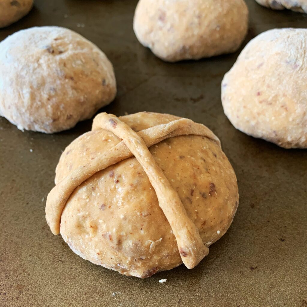 close up view of unbaked hot cross bun on a baking sheet