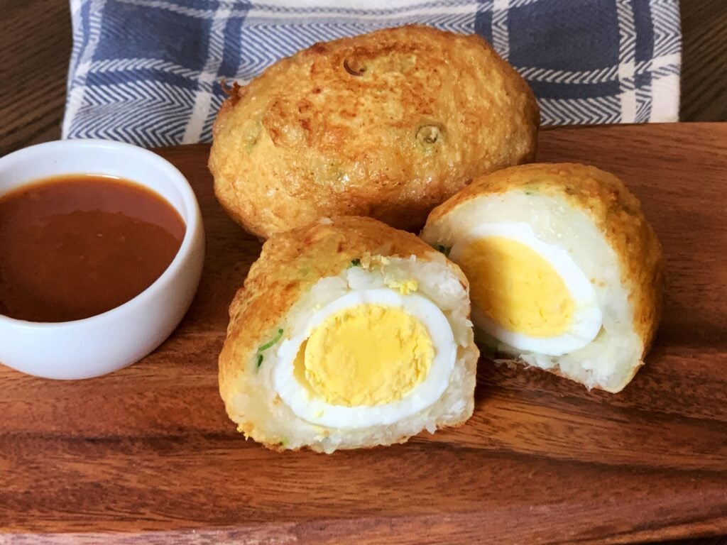 Two cassava egg balls with mango sour on a brown wooden plate. One of the cassava egg balls in cut in half showing the round yolk