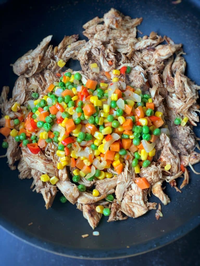 stripped chicken added to sautéed veggies in a pan