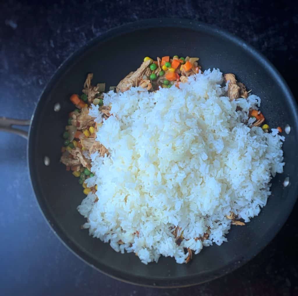 white jasmine rice added to a skillet over chicken and sautéed veggies