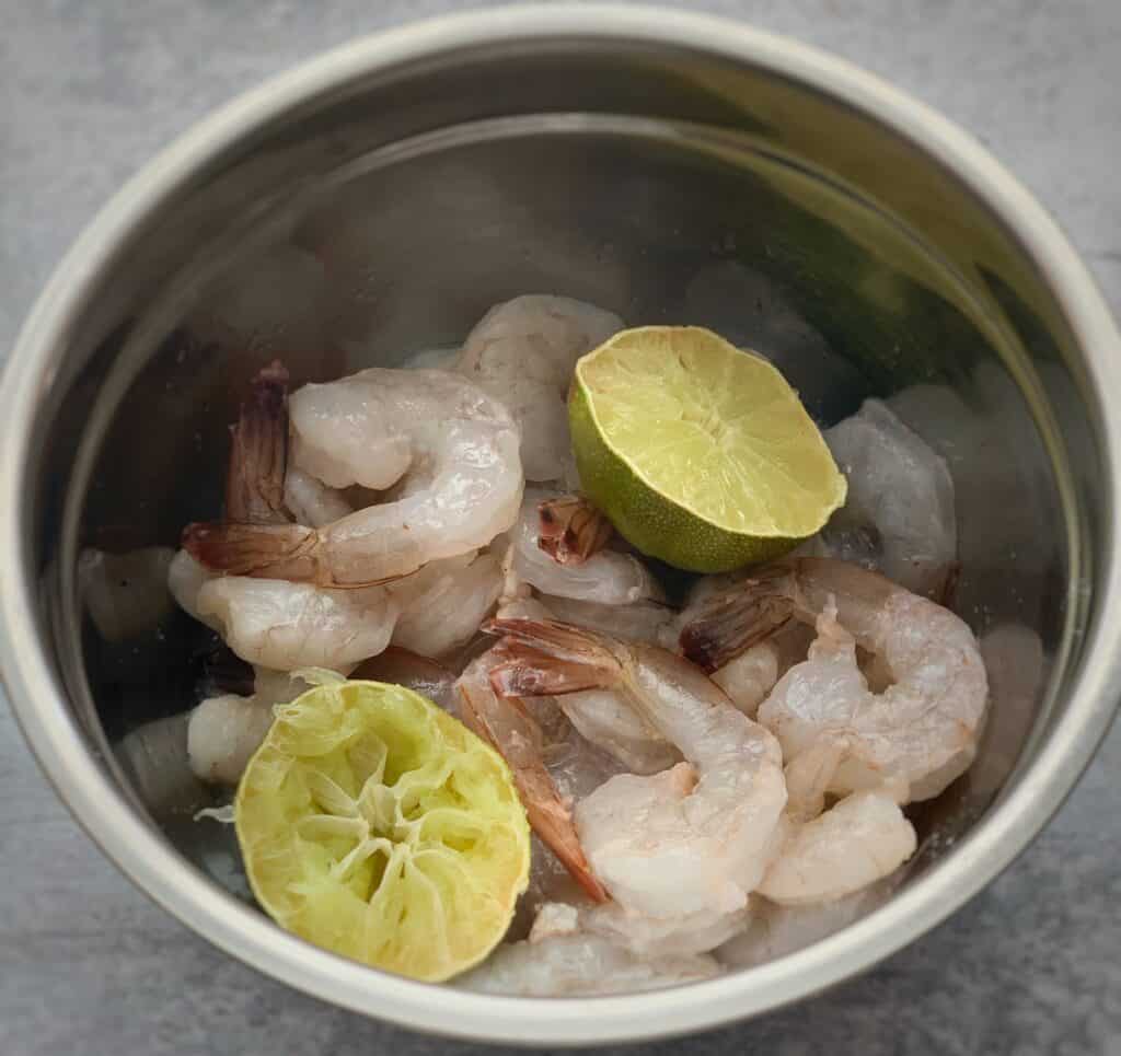 Raw shrimp in a bowl with limes cut in half