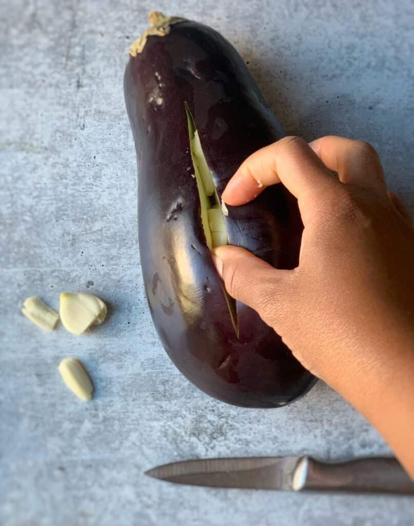 a hand inserting cloves of garlic into a sliced eggplant 