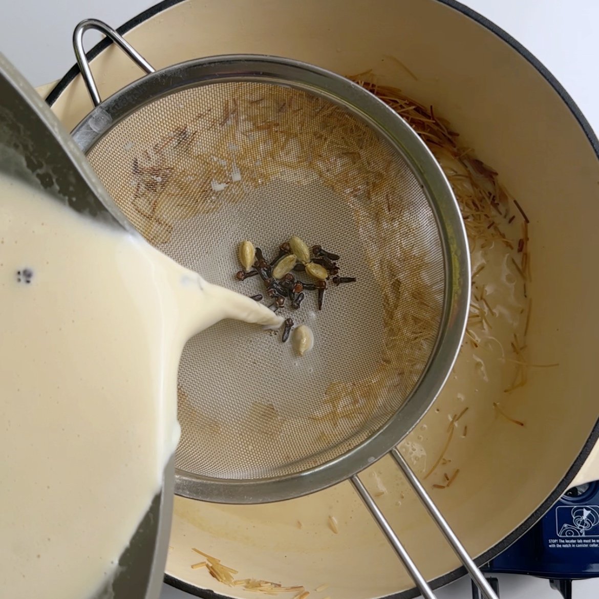 pouring milk through a sieve over a cream pot with vermicelli. Some spices collected in the sieve. 